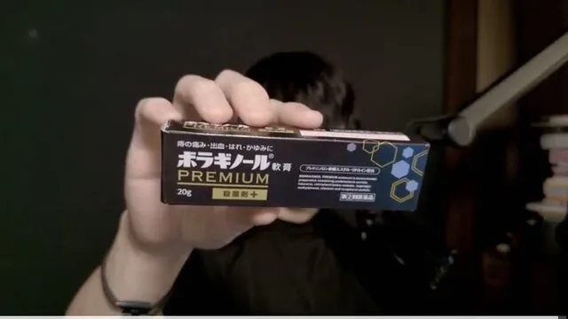室内で、人物が「ボラギノール」の箱を手に持ってカメラに見せている。