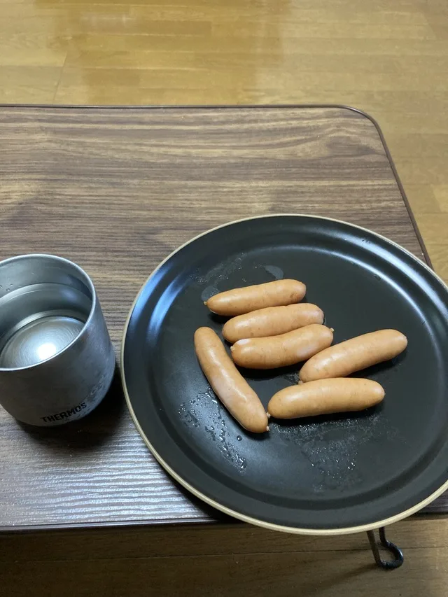 黒い皿に並んだソーセージと、隣に置かれた金属製のカップ。