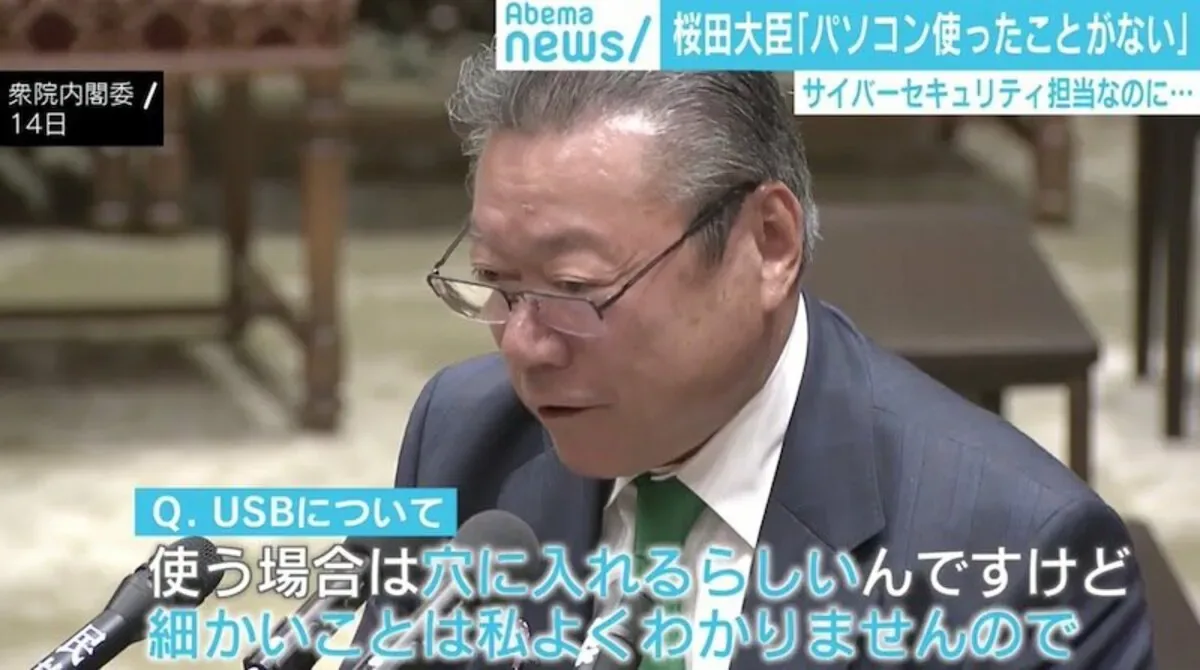 スーツ姿の男性がマイクの前で話している。画面にUSBについての質問と字幕が表示されている。