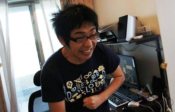 室内で眼鏡をかけた男性が笑顔で座っている様子