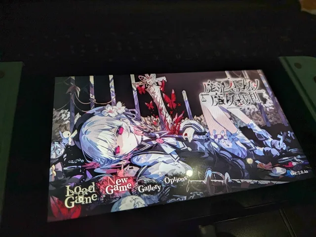 暗い場所に置かれたゲーム機の画面に、華やかな衣装のアニメ風の少女とゲームメニューが映っている。