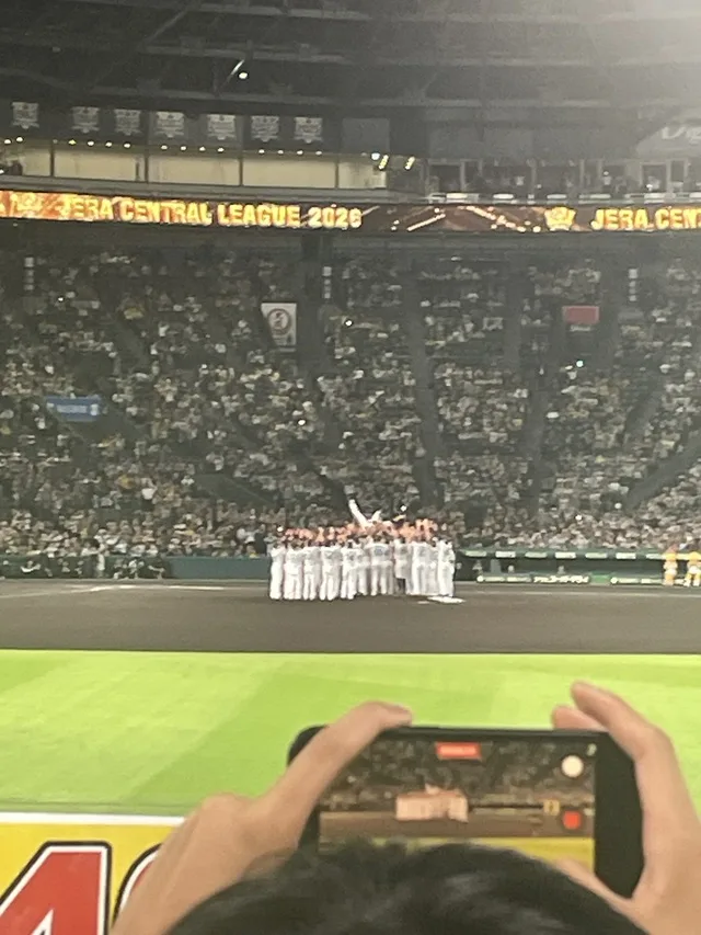 野球場で選手たちが集まり、観客がスマートフォンで撮影している。