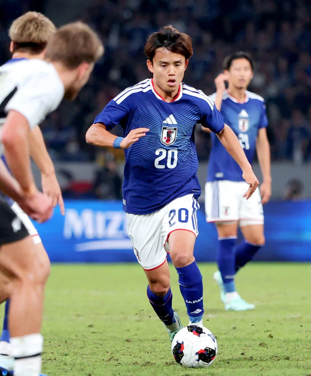 青いユニフォームの日本代表選手が、サッカーの試合中にボールを運んでいる。