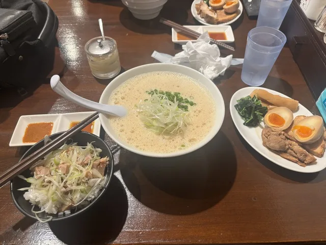 ラーメンとネギ塩丼、煮卵やチャーシューなどの料理がテーブルに並んでいる