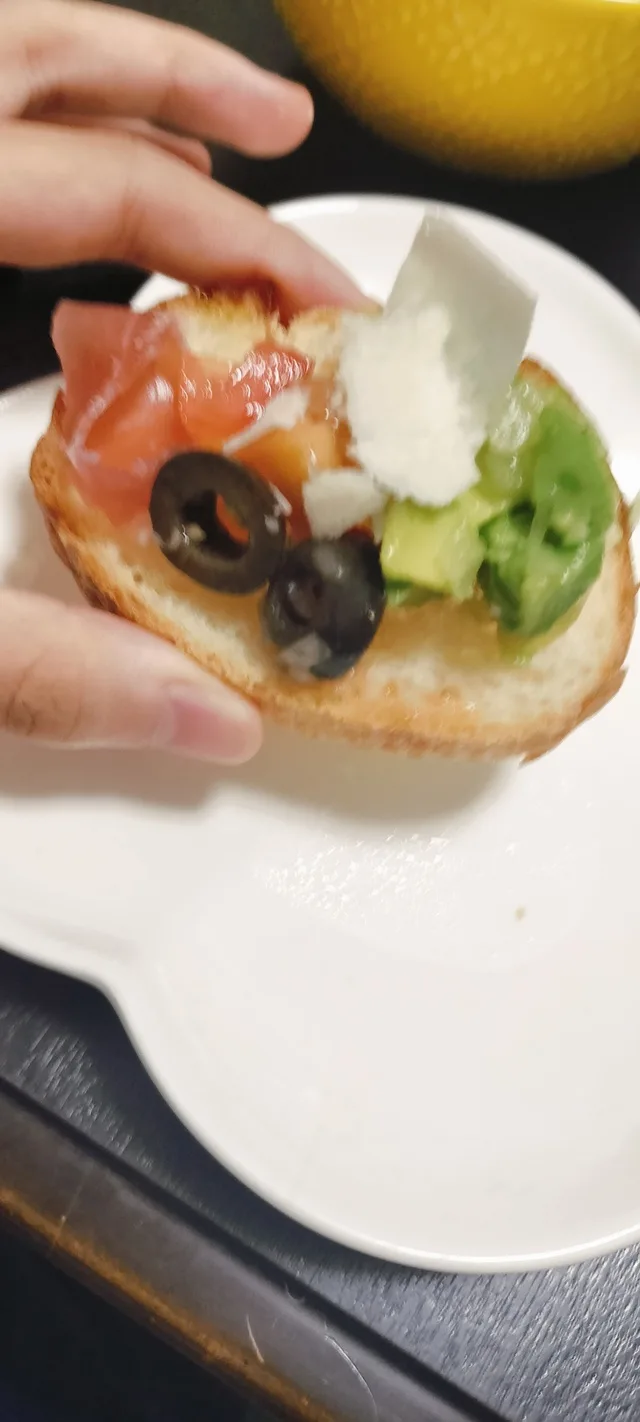 手で持った、トマトやアボカド、オリーブなどをのせたパン